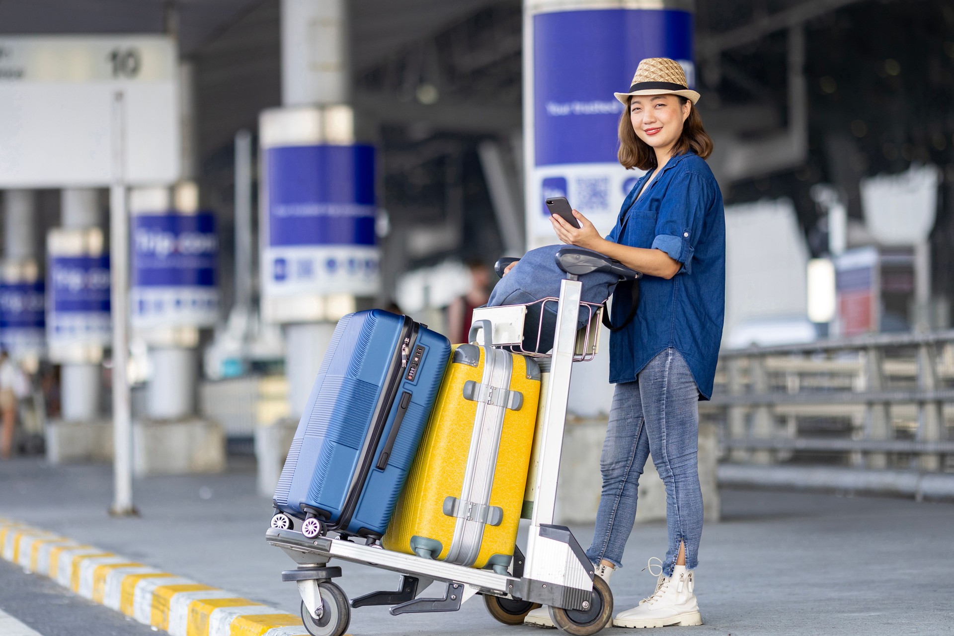 Asian woman tourist passenger is using mobile application to call pick up taxi at the airport terminal for transportation during her vacation travel and long weekend holiday