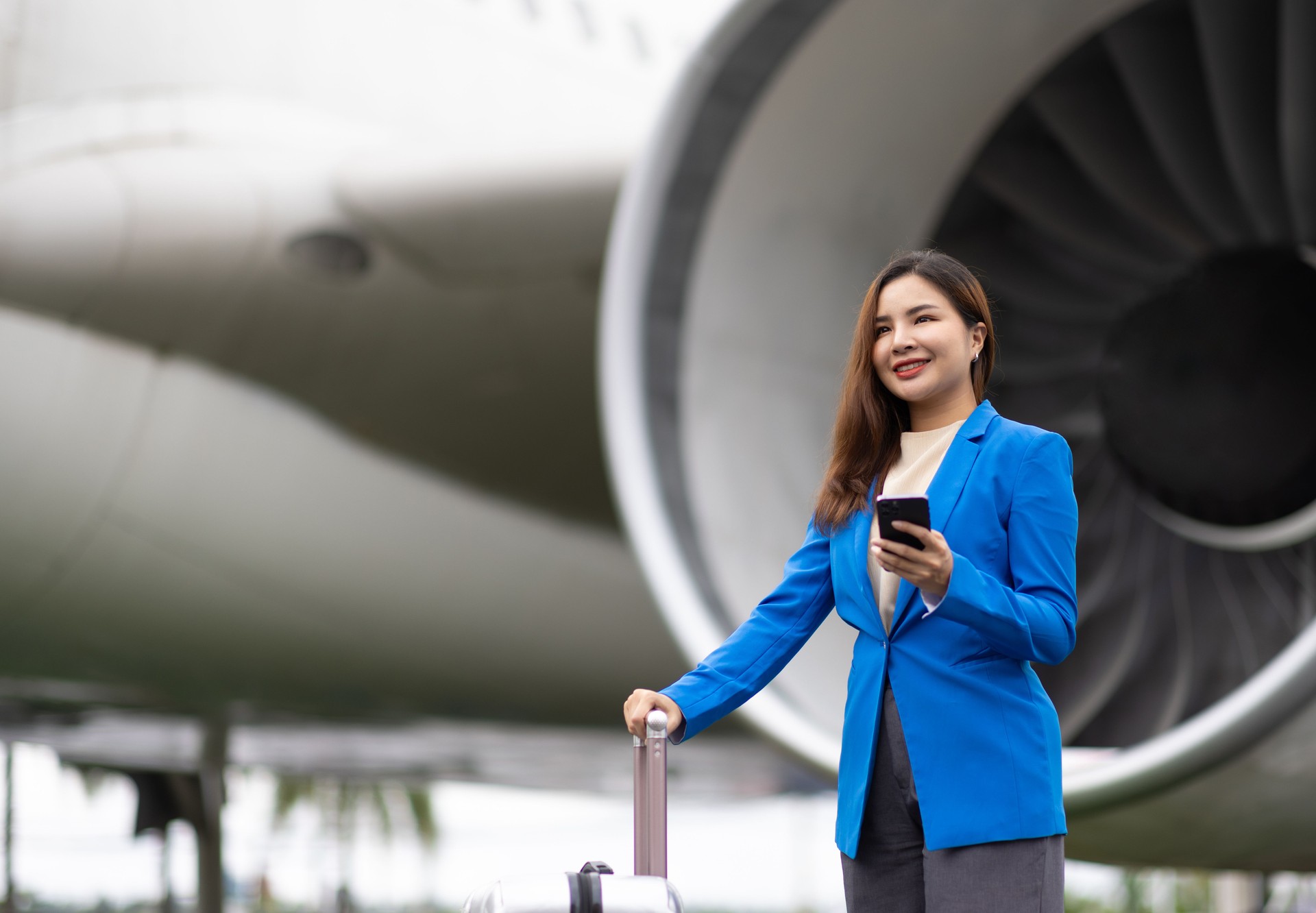 Businesswoman at the airport carries a suitcase, prepares to board the plane and depart. Asian female tourist at airport using smartphone to contact someone.